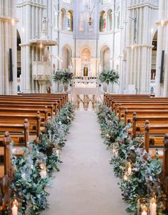 an aisle lined with candles and greenery in front of a church pews filled with flowers