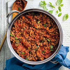 a large pot filled with lots of food on top of a wooden table next to a spoon