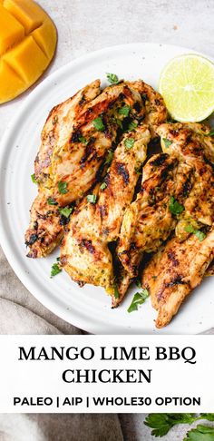 a white plate topped with grilled chicken next to sliced mangoes and lime wedges