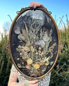 a woman holding up a painting in front of her face with flowers and butterflies on it