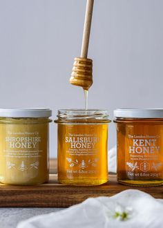 three jars of honey sitting on top of a wooden table