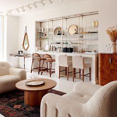 a living room filled with furniture next to a tall glass wall mounted shelf full of bottles