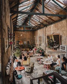 people are sitting in chairs and tables inside an old building with exposed ceilings, windows, and glass doors