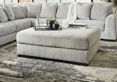 a living room with a couch, ottoman and coffee table in front of a window