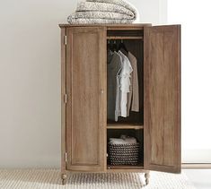 a wooden cabinet with clothes hanging on it's sides and a basket next to it