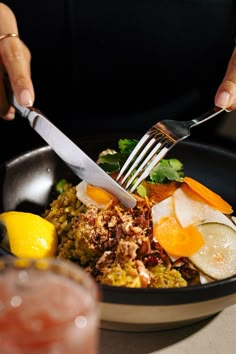 a person holding a fork and knife over a bowl of food