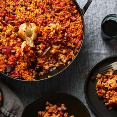 a pan filled with rice and vegetables next to two black plates on top of a table