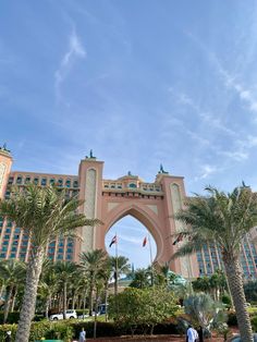 people walking in front of the entrance to an elaborately designed hotel with palm trees