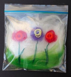 there are three flowers in the plastic bag on the black surface, and one is made out of yarn