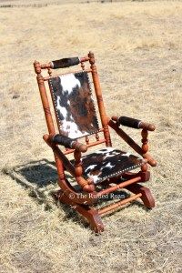 an old rocking chair with a cow hide on it's back in the middle of a field