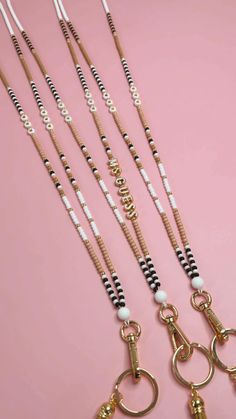 five different types of necklaces on a pink surface with gold and black beads hanging from them