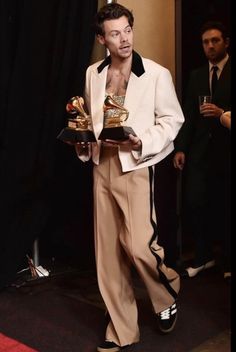 a man standing in front of a black curtain holding two awards and looking at the camera