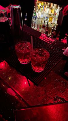 two glasses sitting on top of a bar with red lights in front of the bar