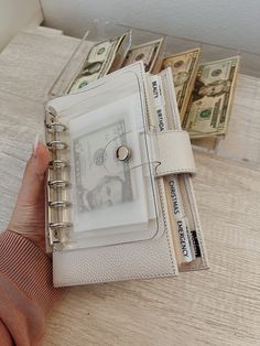 a person is holding a small wallet with money in it and there are stacks of bills behind them