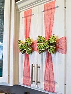 two green and pink bows are hanging on the front door of a white kitchen cabinet