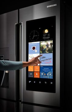 a woman pointing at the touch screen on a stainless steel refrigerator that is built into the wall