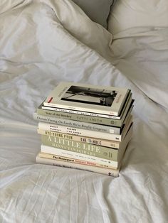 a stack of books sitting on top of a white bed covered in sheets and pillows