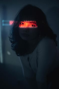 a woman with dark hair and red light on her eyes is staring at the camera