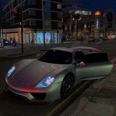 a silver sports car is parked on the side of the road at night in front of some tall buildings