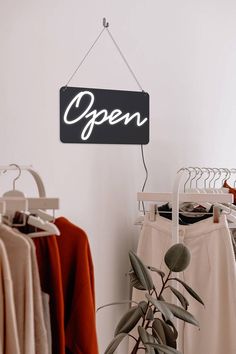 an open sign hanging on the wall next to clothes