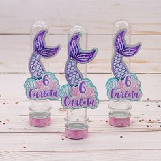 three little mermaid cupcake toppers with purple and blue designs on them, sitting next to each other