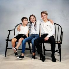 three children sitting on a black chair posing for a photo with their arms around each other