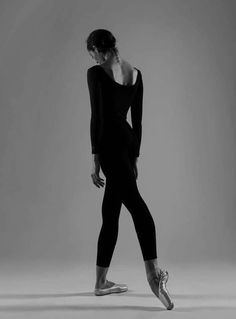 a woman in black leotard and ballet shoes is standing with her back turned to the camera