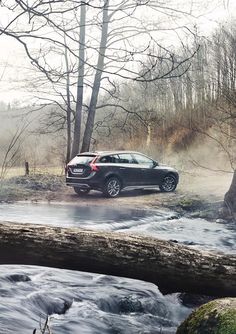 a black car is parked on the side of a river in front of some trees