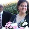 a woman standing next to a man in a suit and tie with flowers on his lap