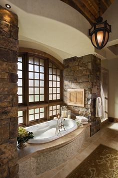 a bathroom with stone walls and large tub in the center, along with two windows