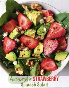 a white bowl filled with spinach, strawberries and avocado on top of a table