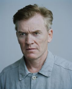 a man in a gray shirt looking at the camera with an intense look on his face