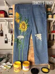 a pair of jeans with sunflowers painted on them next to paint cans and cups