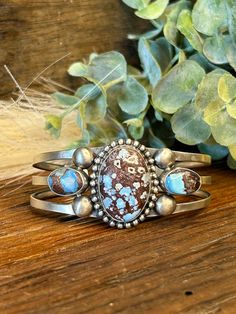 This Stunning Triple Shank Cuff Bracelet is made by Navajo Silversmith Artist Donovan Skeet with unique matrix of Sky Blue and Browns Golden Hills Turquoise stones.  Theses oval stones are set in a smooth sterling bezel and the large center stone is surrounded by pearl beading.   Golden Hills Turquoise is mined in the Altai Mountains in Kazakhstan.  It is believed to promote positive energy, emotional balance, and overall well-being making this ring the perfect gift for a friend or spouse for any special occasion! ★Specifics★ Metal: Sterling Stamped Size of Bracelet: As the piece sets it will fit a 6 1/4" wrist and can be slightly adjusted up or down. Gap: 1" Width: 1 1/8" at widest point on the setting, 3/8" at most narrow point Setting overall with all stones: 2 1/8"w x 1 1/8"h Weight of Altai Mountains, Pearl Beading, Golden Hill, Turquoise Bracelet Cuff, Emotional Balance, Turquoise Stones, Bracelet Cuff, Oval Stone, Bracelet Jewelry