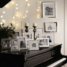 a piano with pictures and candles on it in front of a christmas light garlanded wall