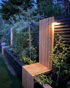 a wooden bench sitting in the middle of a lush green garden at night with lights on