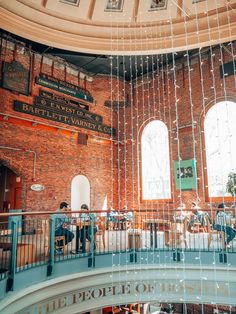 the inside of a building with people sitting at tables and standing in front of large windows