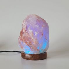 a pink and blue rock sitting on top of a wooden stand next to a black cord