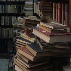 many books are stacked on top of each other in a room with shelves full of books