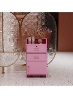 a pink file cabinet sitting in front of a gold and glass table with candles on it