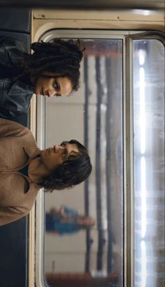 two women standing next to each other in front of a window on a subway car