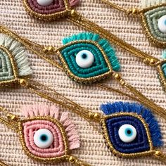 several different colored evil eyes are hanging from gold chains on a piece of fabric with beads