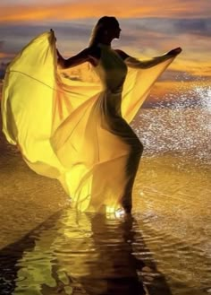 a woman in a yellow dress is walking on the beach with her arms spread out