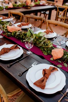 the table is set with white plates and napkins, silverware, and greenery