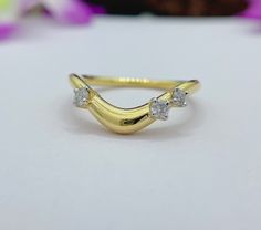 a yellow gold ring with three diamonds on it's side, sitting on a white surface