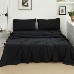 a bed with black sheets and pillows in a white room