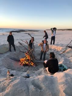 several people standing around a campfire on the beach