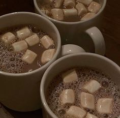 three mugs filled with hot chocolate and marshmallows on top of a table