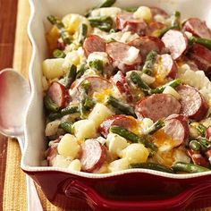 a casserole dish with sausage, potatoes and asparagus on a place mat