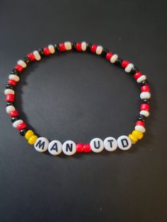 a beaded bracelet with the word man written on it in white, red, yellow and black beads